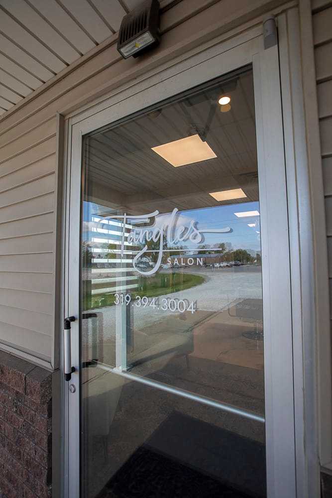 Glass door with "Tangles Salon" logo and phone number, reflecting outdoor view.
